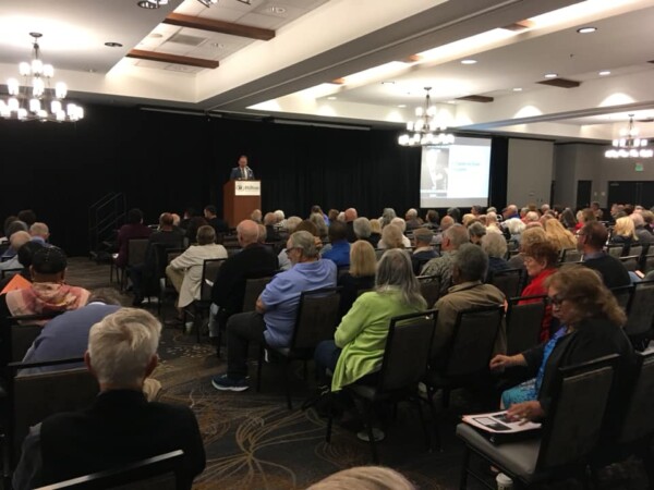 A hotel room is packed with people sitting in chairs listening to an attorney present estate planning updates.