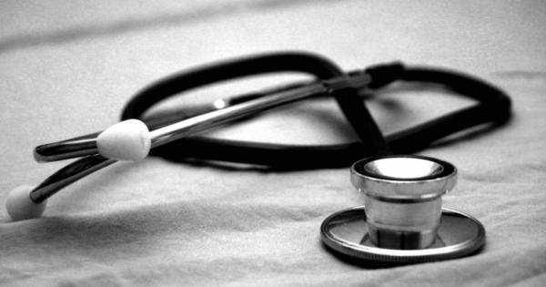 A black and white photo of a stethoscope sitting on a flat surface.