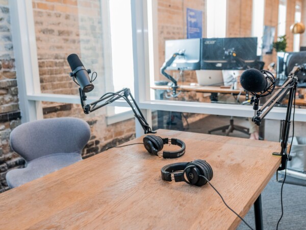 A grey chair sits behind a wooden table. On the table sit recording equipment including a black microphone and black headphones.